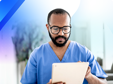 Healthcare professional in blue scrubs and glasses using a tablet in a medical setting