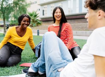 Group of students sitting on the grass outdoors, laughing and talking together on campus