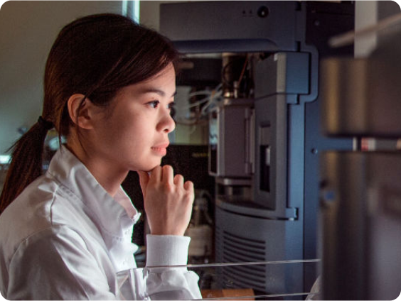 白衣を着た集中力のある女性科学者が、高度な科学機器に囲まれた薄暗い実験室でコンピューターに向かっている。