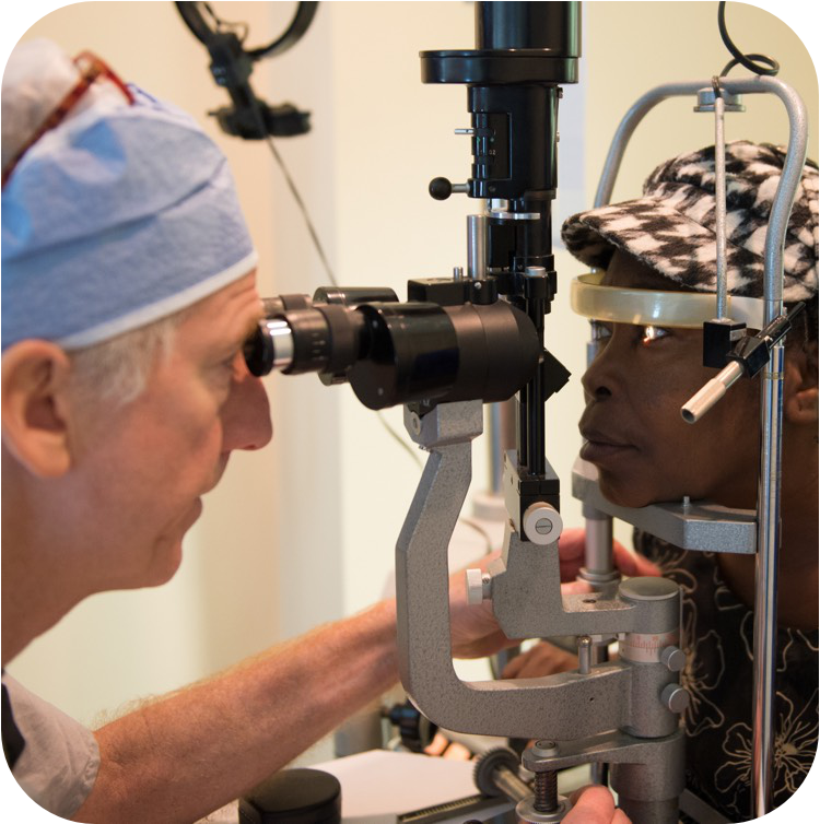 Un médecin portant un bonnet chirurgical bleu clair effectue un examen de l'œil à l'aide d'un biomicroscope à lampe à fente. La patiente pose son menton sur le support de l'appareil et regarde droit devant elle.